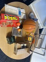 Photo of table with miscellaneous office supplies, games, and sports equipment including mini basketball set, calculator, puzzle games, papers, and CDROM discs.
