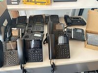 Thirteen used IP desk phone bases arranged on table including Black Polycom, RingCentral and Yealink units