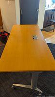 Top view of rectangular wooden desk surface with central inset power outlet panel.