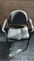 Single black chair with rounded backrest and armrests, black metal frame, and vinyl seat and backrest.