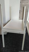 Photo showing the underside of white rectangular table with four straight legs against a wall with brick and painted sections.