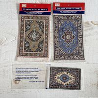Three miniature Turkish woven carpets displayed flat on a white surface with original branding labels. Two larger carpets and one smaller carpet shown with detailed floral medallions and traditional patterning.