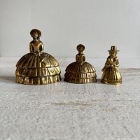 Front view of three vintage brass southern bell crinoline girl figurine bells arranged in a row
