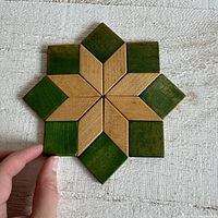 Top view of the star-shaped wood trivet showing beige and green geometric pieces forming a star pattern on a textured white surface.