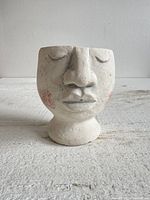Front view of a small off-white ceramic planter shaped like a closed-eyed head with rosy cheeks.