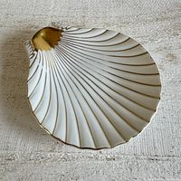 Top-down angled view showing the shell shape, white ceramic surface, gold detailing on shell opening and edges.