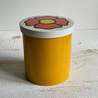 Side view of yellow enamel storage container with white lid decorated with a red-orange flower design.