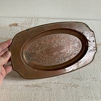 Front facing photo showing the intricate etched floral and scroll pattern on the oval copper trinket dish held in a hand.
