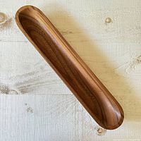 Full view of vintage solid wood long skinny tray bowl on textured fabric surface, showing elongated shape and wood grain.