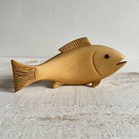 Front view of vintage light wood fish carving with etched fins and tail, open mouth and dark eyes, sitting on a surface.