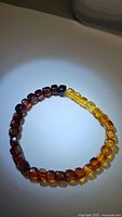 Photo of a stretchy Baltic amber bracelet with gradient bead colors ranging from dark red to yellow, on white background under spotlight.