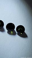 Three round, faceted green tourmaline gemstones placed in a row on a white surface under direct light, showing color and clarity.