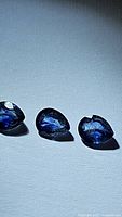 Three pear-cut blue sapphires aligned on a white surface showing facets and natural color.