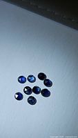 Nine small, round blue sapphires with fancy rose cut, arranged on a white background, showing their deep blue color and rose cut facets.