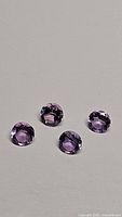 Four natural round-cut purple amethyst gemstones on gray background, showing their size and color.