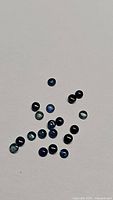 Photo showing multiple small round cabochon natural blue sapphires in light and dark shades arranged on white background.