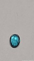 Oval cut blue topaz gemstone with facets reflecting light, unique blue-green color visible.