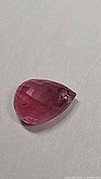 Close-up of the 1.40ct red ruby gemstone showing faceted Fancy Briolette cut and drilled hole for jewelry use.
