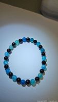Photo of natural black onyx and ocean blue agate bead stretchy bracelet laid flat on light surface showing round polished beads in alternating colors and patterns.