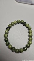 Full view of the natural green jade bead stretchy bracelet placed on a light surface.
