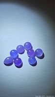 Ten natural lavender chalcedony cabochons arranged on a flat surface with visible variations in shape and size under light.