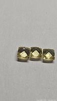 Three small, square cushion-cut lemon citrine gemstones arranged in a row on a plain white background.