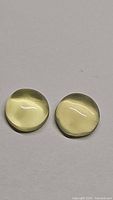 Close-up of two round cabochon cut lemon citrine gemstones showing their smooth domed surface and pale yellow color.