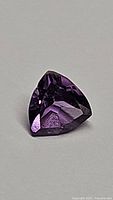 Natural purple amethyst gemstone, trillion cut, shown in clear lighting on white background.