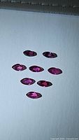 Eight marquise cut deep red pink rubies displayed on white surface, showing vibrant color and facets.
