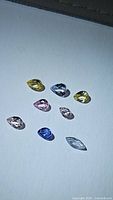 Photo showing nine natural multicolored pastel sapphires arranged on a white background.