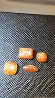 Photo showing 4 pieces of natural sunstone gemstones with different cuts on black textured background showing their glittering sparkles.