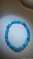 Ocean blue agate stretchy bracelet laid flat showing round beads with hues of blue and some white bands under soft lighting.