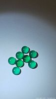 Photo showing nine round vivid green onyx cabochon gemstones with polished smooth domed surfaces, arranged on a white background.