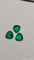 Three vivid green onyx gemstones in trillion cut shape shown on a neutral background under bright light revealing their color and clarity.