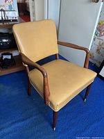 Yellow vinyl upholstered accent chair with wooden frame and armrests. Legs have brass caps.