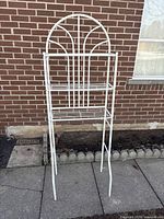 White metal bathroom storage rack with three shelves standing outside against brick wall