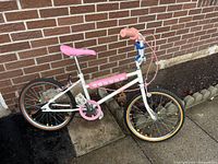 Children's 19 inch bike against brick wall, white frame with pink grips and saddle, blue front fork, colored spoke reflectors, shows light use