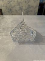 Closed crystal candy jar with pointed finial lid on floral tablecloth.