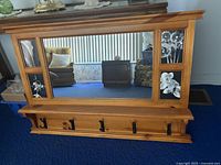 Front view of wooden photo frame with central mirror, four photo openings, a shelf, and five black metal hooks below.