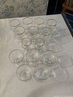 Front angled view of all 14 glasses arranged on a white surface showing clear glass with gold rims and various bowl shapes.