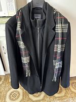 Full view of black double layer men's coat displayed on hanger with black, white, and red checkered scarf attachment visible on the coat lapels.