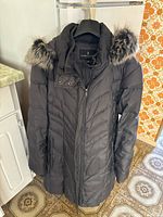 Full front view of black London Fog women's winter coat with fur-trimmed hood hung on hanger, showing quilted detail and buttoned flap over zipper.