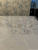 Set of five clear martini glasses arranged on a table with wallpaper background. Ribbed texture and flower etching visible.