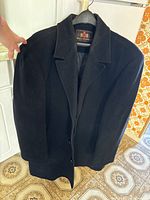Front view of the black men's coat hanging on a hanger, showing the lapel collar and full length.