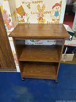 Front angle of the wooden office side table showing top and two shelves with caster wheels.