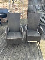 Two outdoor woven wicker reclining chairs viewed from front on wooden deck, showing straight backs and armrests.