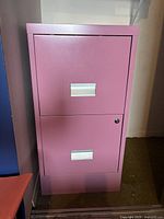 Pink 2-drawer metal filing cabinet with silver recessed handles and lock on top drawer.