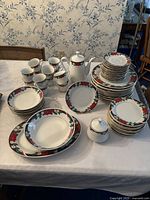 Photo showing the full poinsettia china set including multiple plates stacked, teacups, a teapot, and a sugar bowl all decorated with red poinsettias and green holly leaves with gold rims.