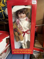 Porcelain doll in original Sears box, dressed in white knit dress, holding teddy bear.