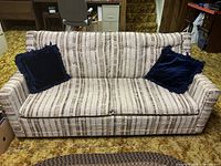 Front view of a striped pattern pull out couch with two navy blue cushions on a carpeted floor in a room setting.